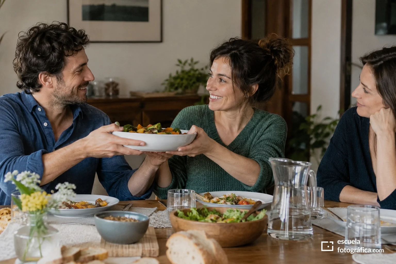 Dos personas se pasan una fuente mientras conversan en la mesa
